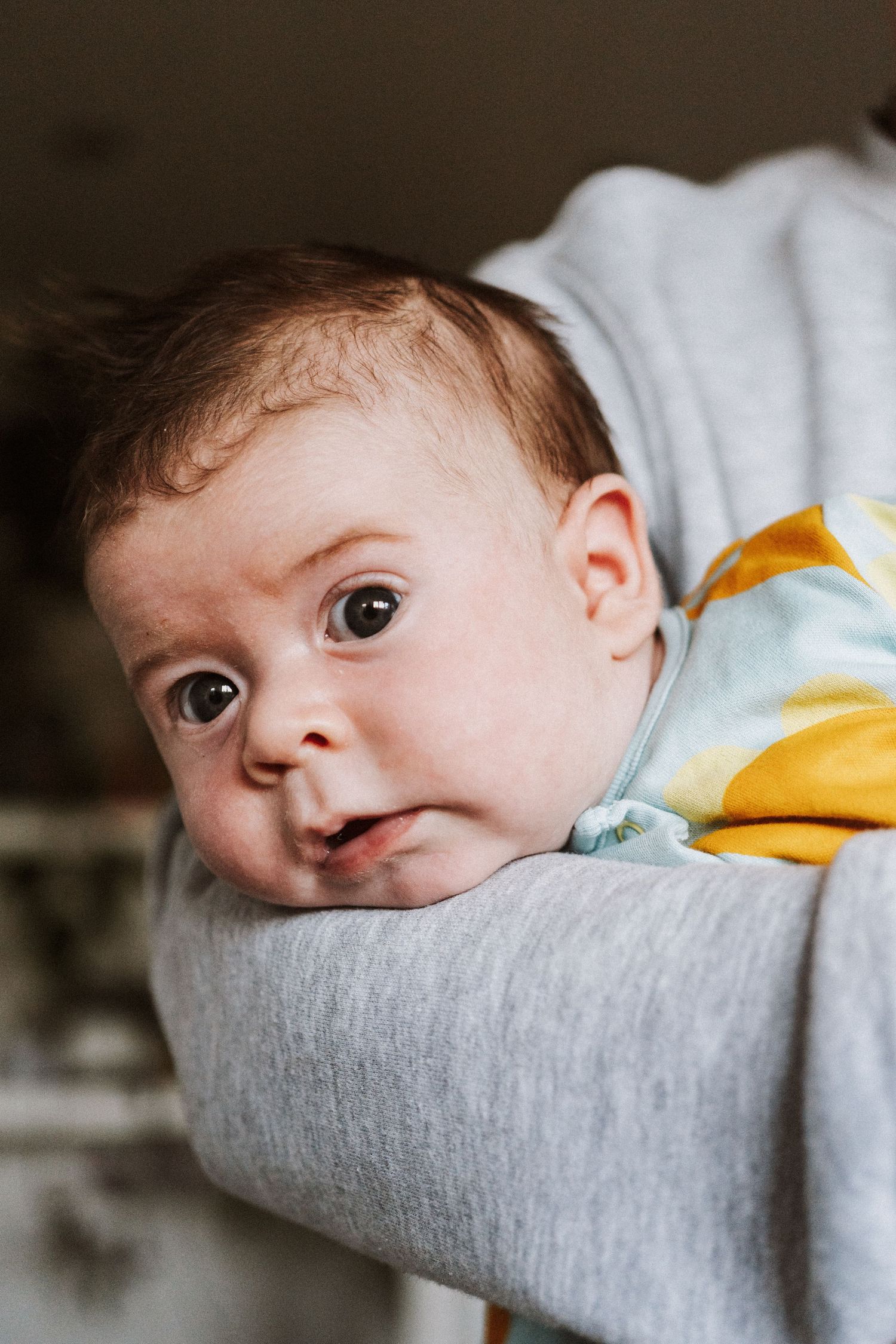A baby peeks over the edge of a gray cushion in a series of similar photos showing different angles.