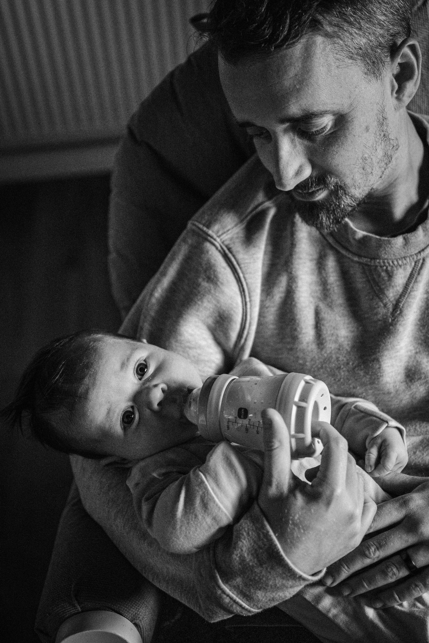 A tender black and white portrait of a parent bottle feeding a baby in a quiet, intimate moment.