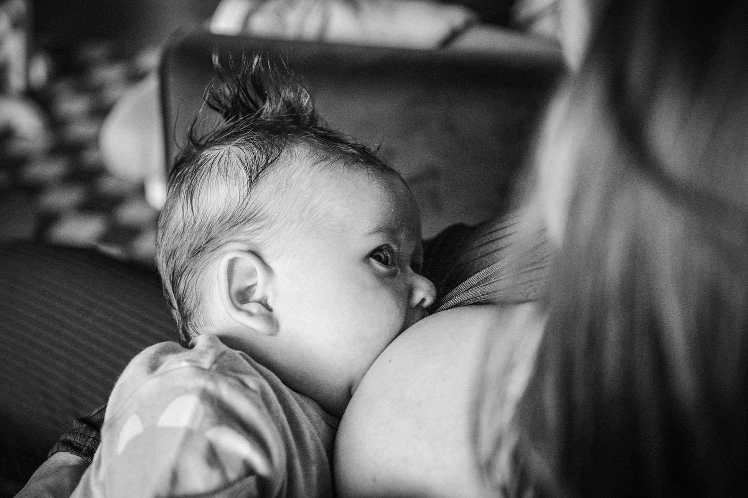 Black and white photograph of a sleeping infant lying on patterned bedding.