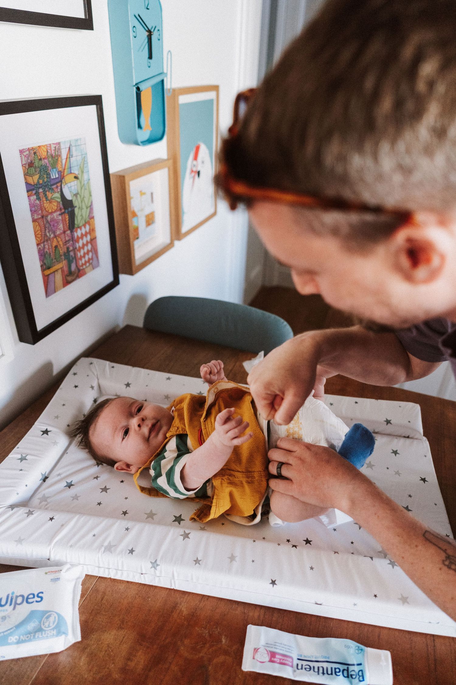 A series of photos showing a baby getting a diaper change on a changing pad while artwork hangs on the wall behind.