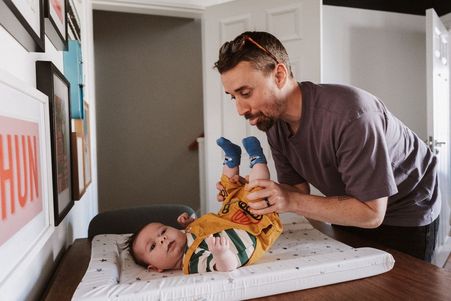 A parent changes a baby's diaper on a changing table while playfully interacting with their child.
