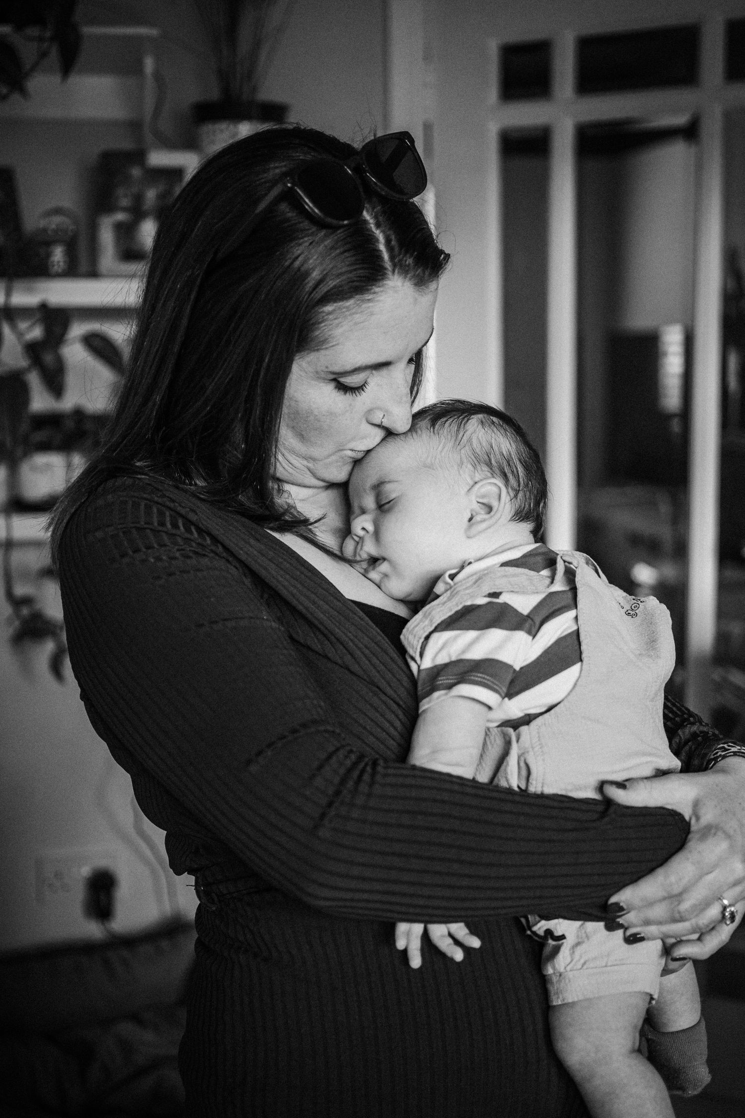 A tender black and white photograph capturing an intimate moment between a mother and sleeping baby in a home setting.