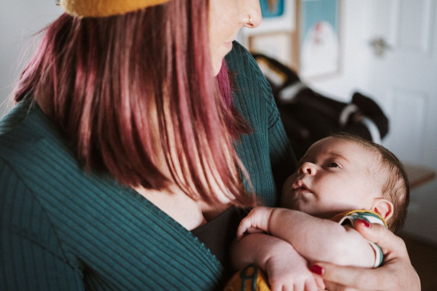 A mother with pink hair holds and comforts her baby in a tender moment.