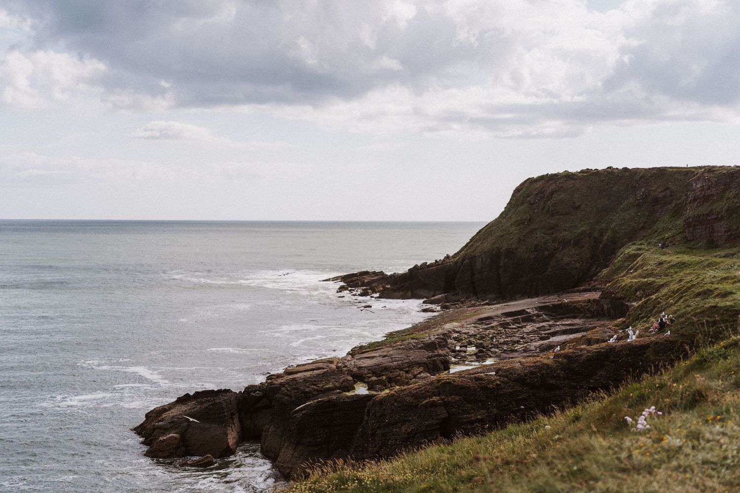 Panoramic coastal landscape showing rugged cliffs and crashing waves along a dramatic rocky shoreline.