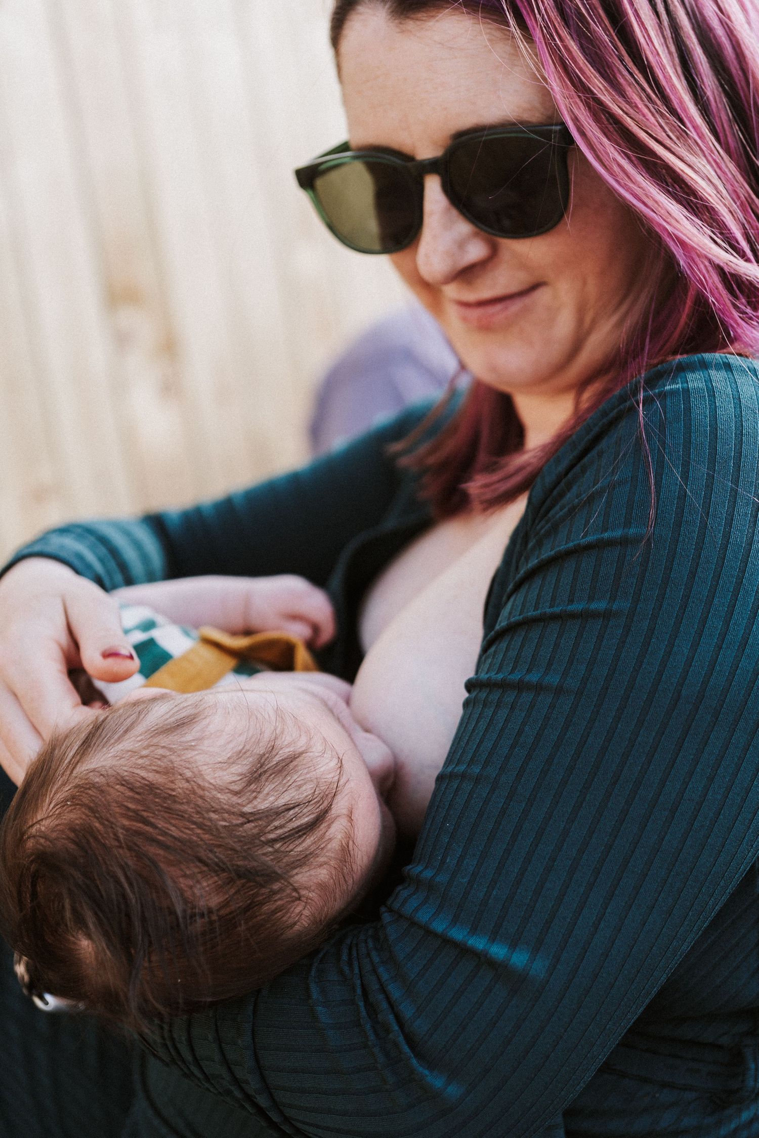Close-up of breastfeeding mother wearing dark sweater and sunglasses while feeding baby.