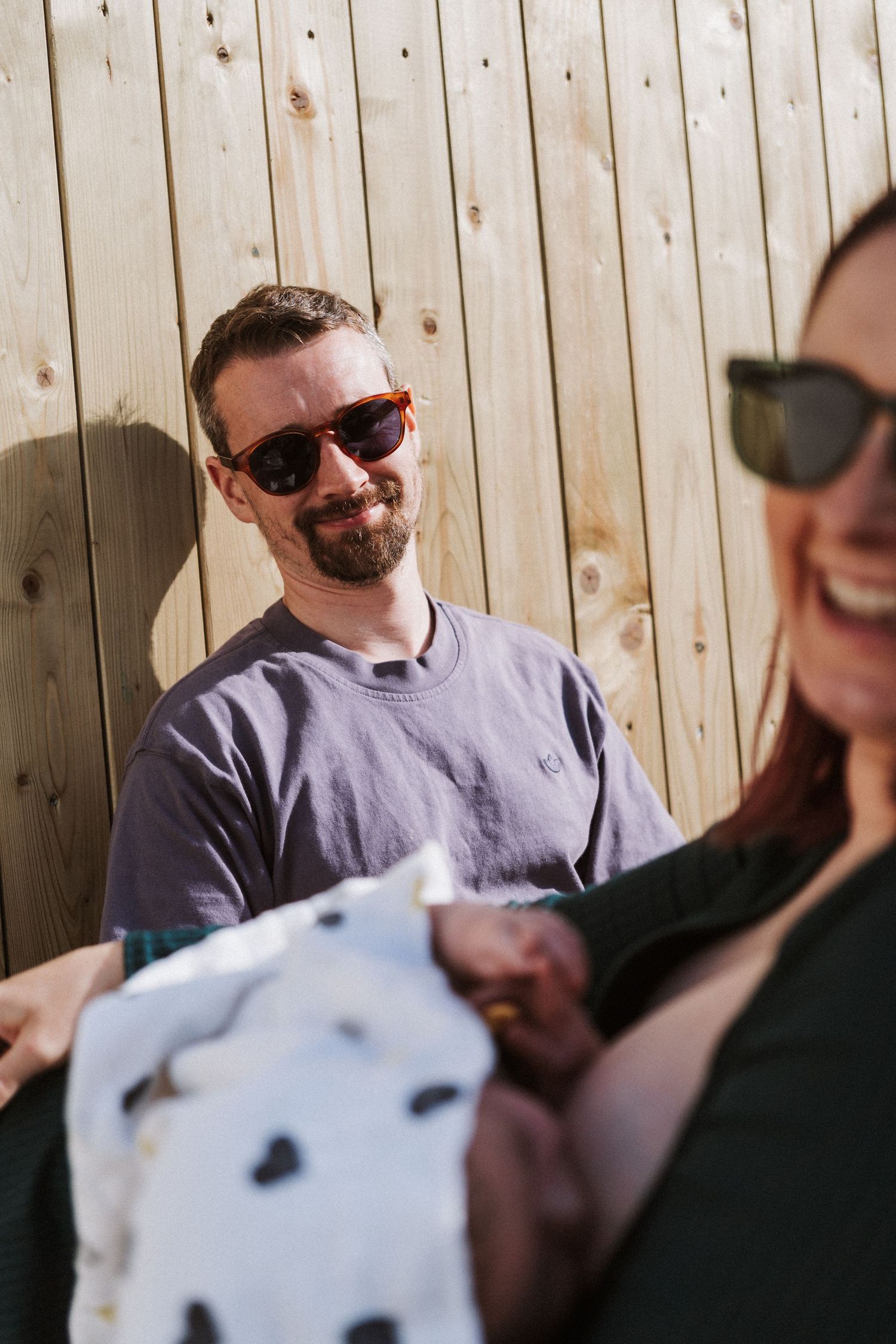 A series of candid photos showing people wearing sunglasses sitting together outdoors against a wooden fence.
