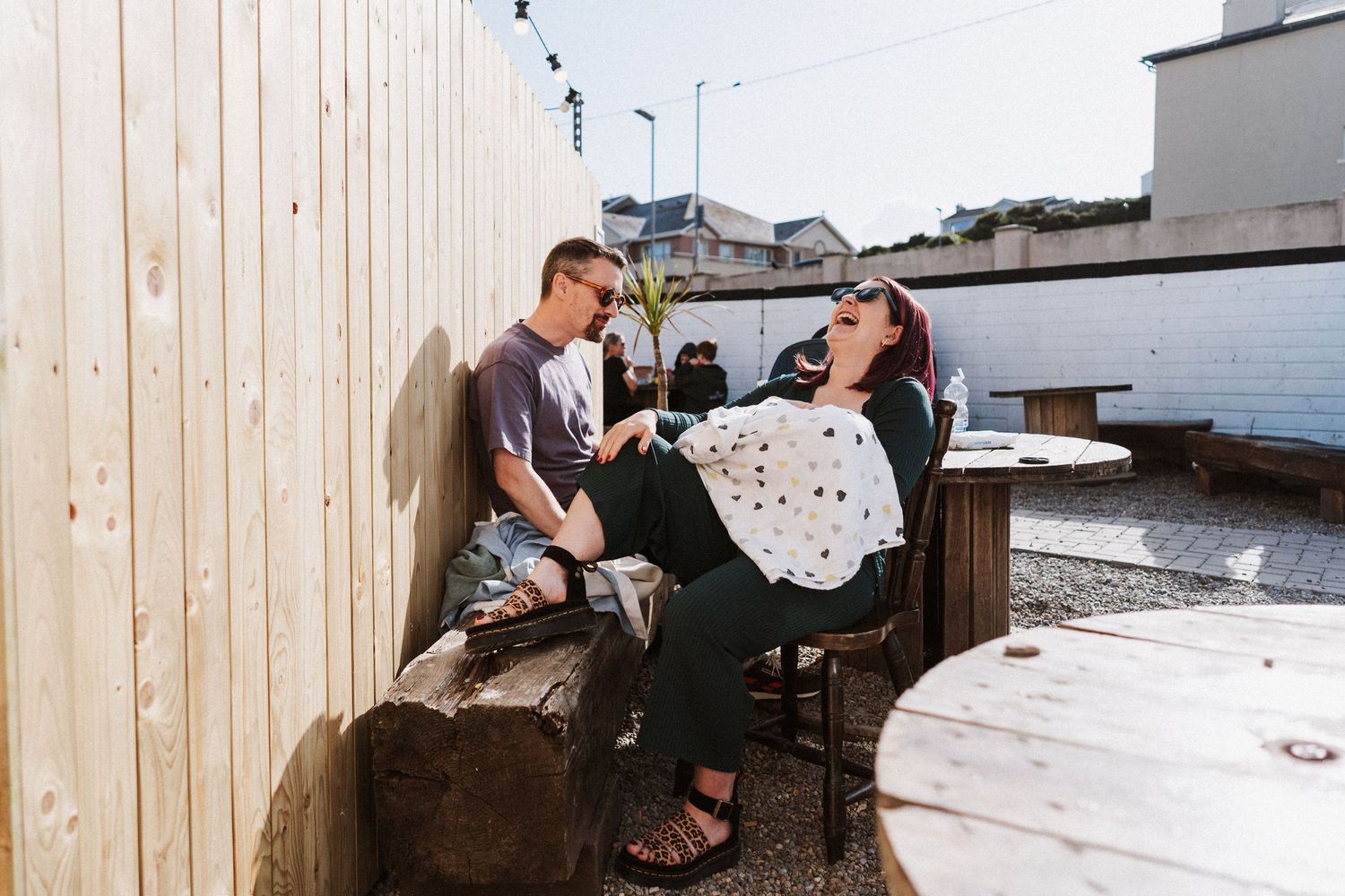 Two people enjoying drinks and conversation on an outdoor rooftop patio on a sunny day.