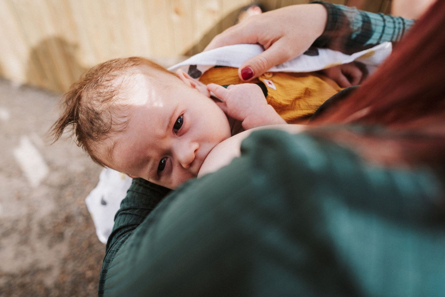 Close-up view of a baby being held in someone's arms while wearing a teal colored outfit.