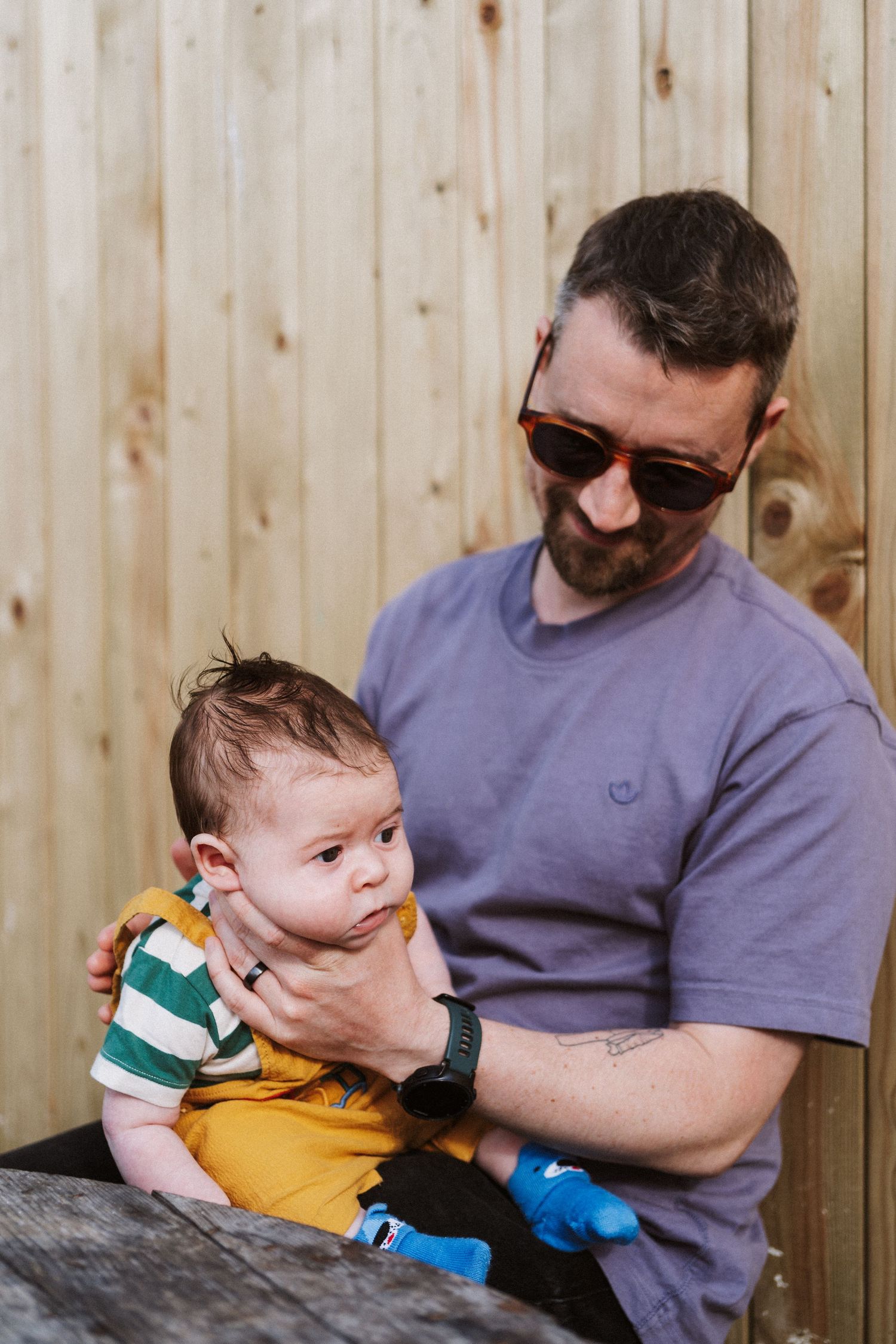 A sequence of four candid photos showing a parent and baby interacting against a wooden fence background.