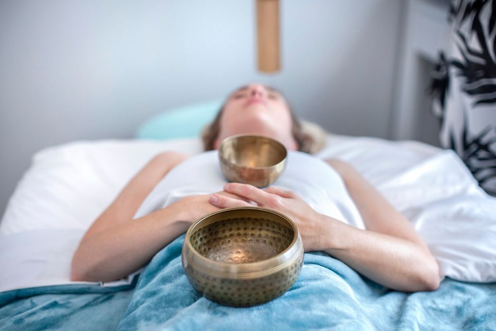 Woman lying on a bed during a Tibetan singing bowl sound healing therapy session for relaxation.