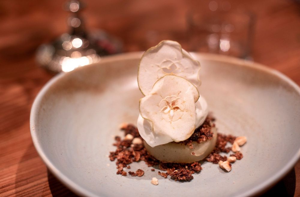 Elegant gourmet dessert with apple slices, cream, and chocolate crumble on a ceramic plate.