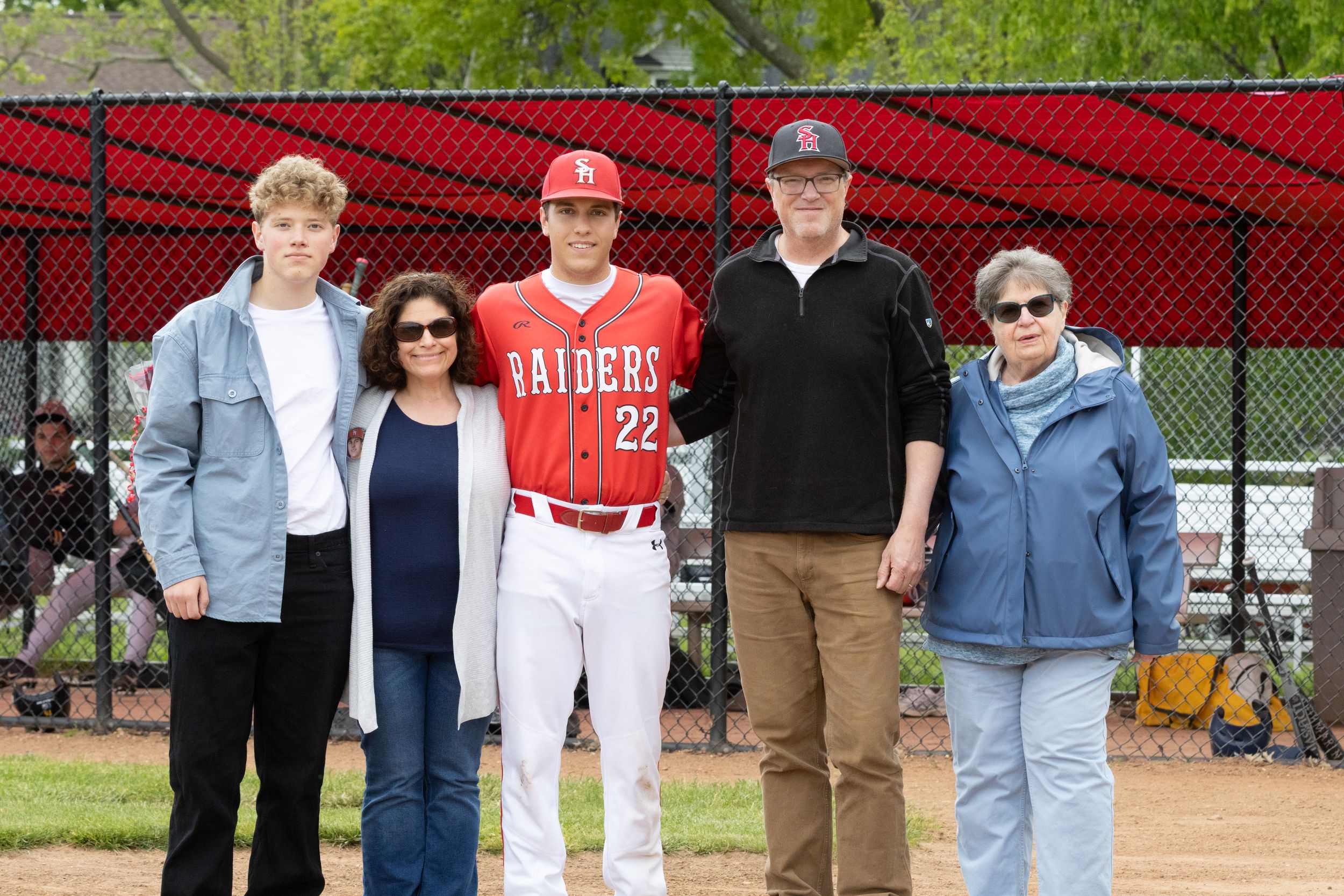 Baseball player in Raiders #22 jersey poses with four family members on senior day at a baseball field.