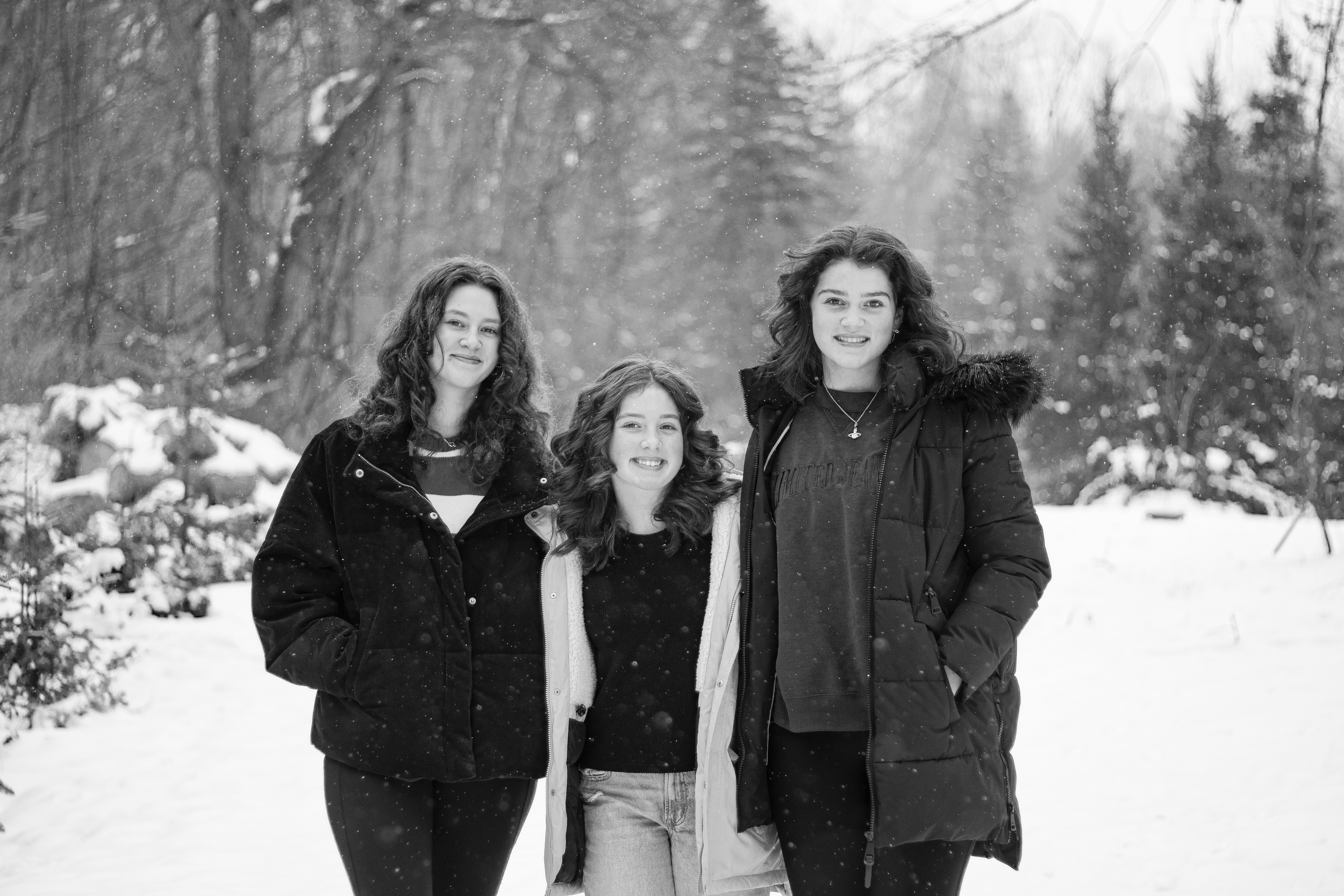 Black and white portrait of three young women smiling together in a snowy outdoor setting during a winter session.