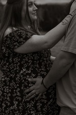 Black and white photo of pregnant woman in floral dress holding partners face in loving embrace taken by Eatonville photographer