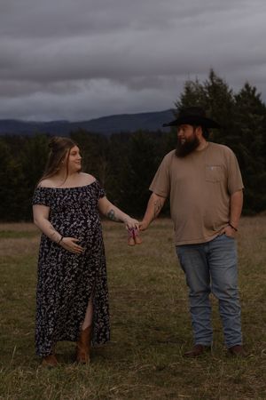Pregnant woman and bearded man in cowboy hat holding hands in an eatonville washington field taken by pierce county photographer