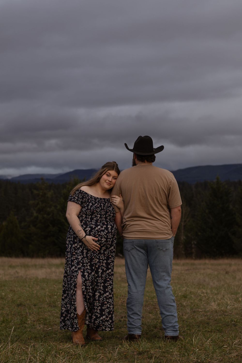 Pregnant woman in floral dress leaning on partners shoulder in a rural field in eatonville washington taken by roy washington photographer