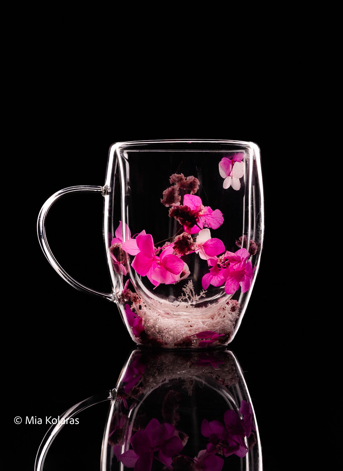 White line photography of a glass that has pink flowers inside, against a black backdrop & a reflective surface