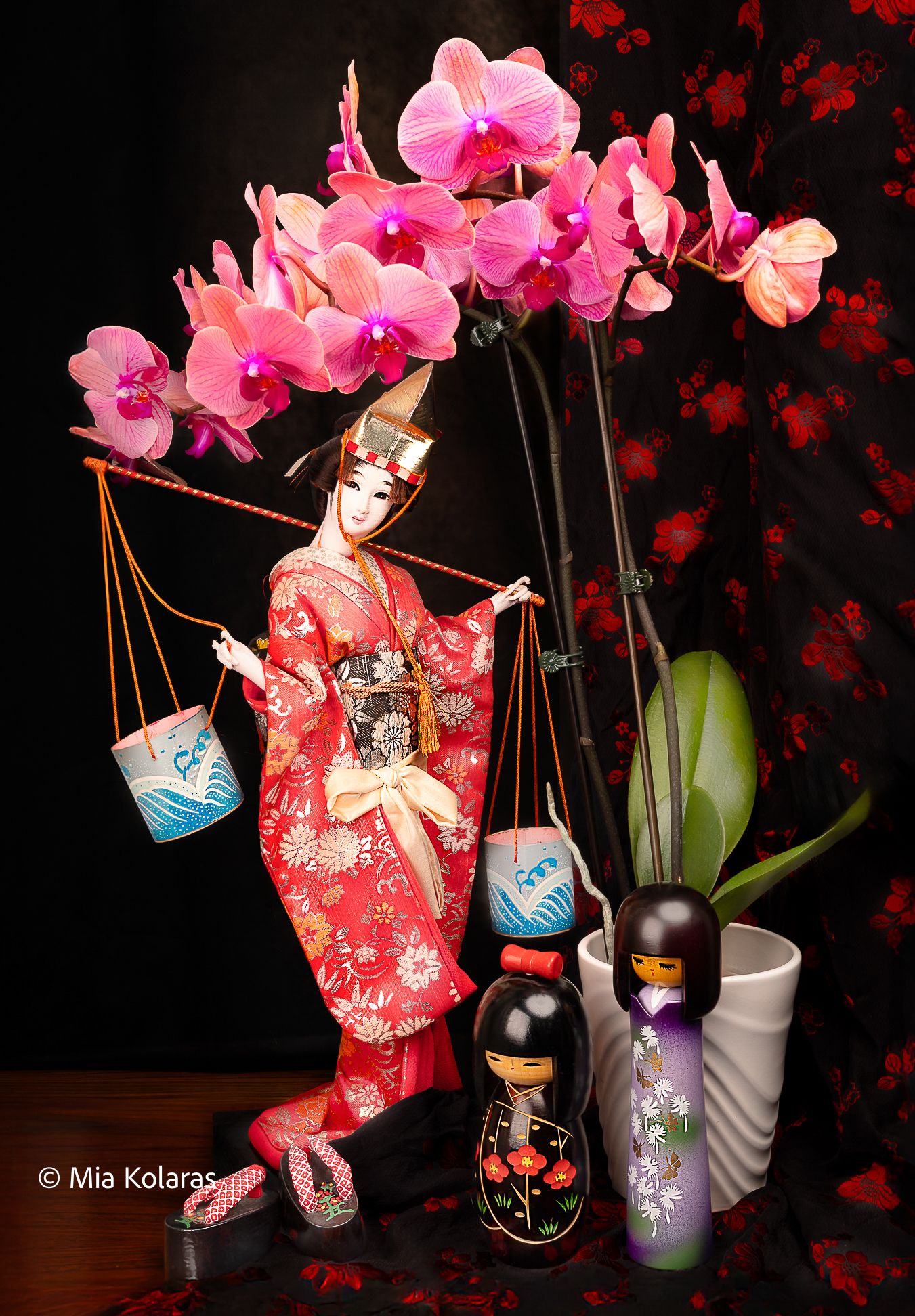Japanese inspired still-life, with a pink orchid, a Geisha doll in a red/pink dress, Geisha slippers, and two Kokeshi dolls