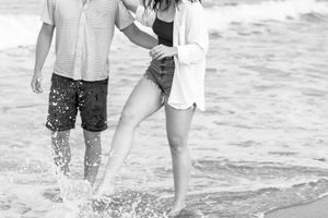 A couple splashing and playing together in the ocean waves at the beach, captured in black and white.