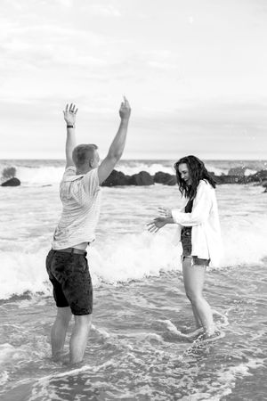 A couple dances and plays in the shallow ocean waves in black and white.