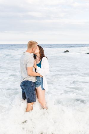 A romantic couple plays in the ocean waves during a beach photoshoot.