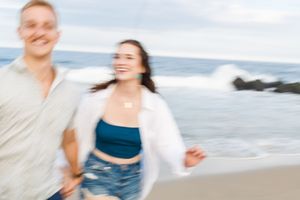 A couple shares a joyful moment together on a bright beach with waves in the background.