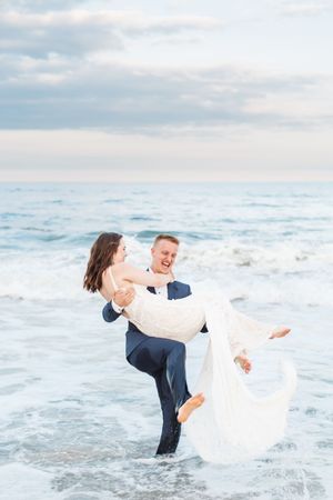 A couple plays in the ocean waves during their beach wedding photoshoot.