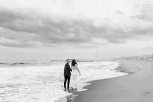 A couple walks along a misty beach shoreline during an overcast day.