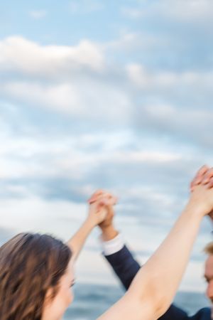 Raised hands against a blue sky with soft white clouds creating a joyful celebration moment.
