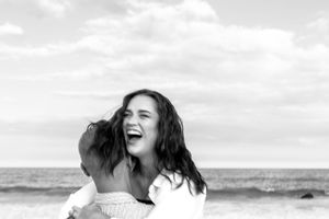 A joyful black and white moment of pure laughter captured at the beach with ocean waves in the background.