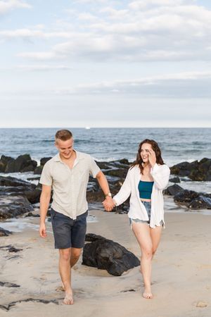 A couple playfully walking and splashing together on a rocky beach at sunset.