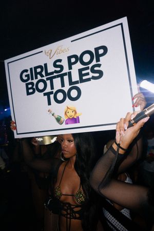 Woman holding a Girls Pop Bottles Too sign at a nightclub party event.