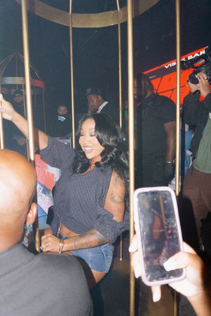 Woman in denim shorts dancing inside a gold cage at a vibrant nightclub event.