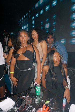 Group of young women posing together at a nightclub with colorful LED lights in the background.