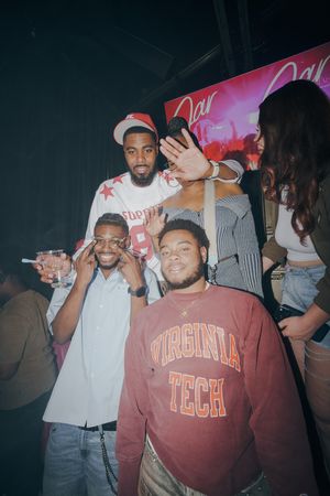Group of friends posing at a party, one wearing a Virginia Tech sweatshirt, at a nightclub event.