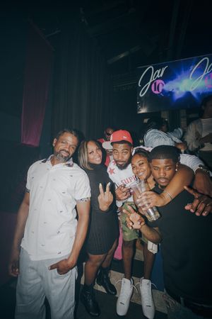 Group of friends posing together at a nightclub event, smiling and making peace signs under neon lights.