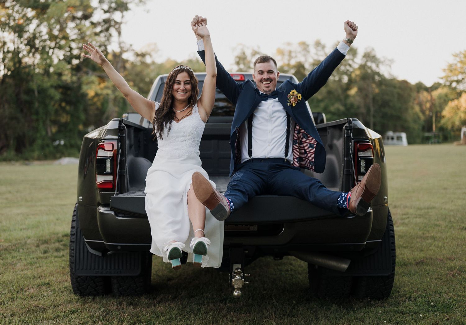 A couple sits in the back of a black pickup truck during a sunset photoshoot in a grassy field.