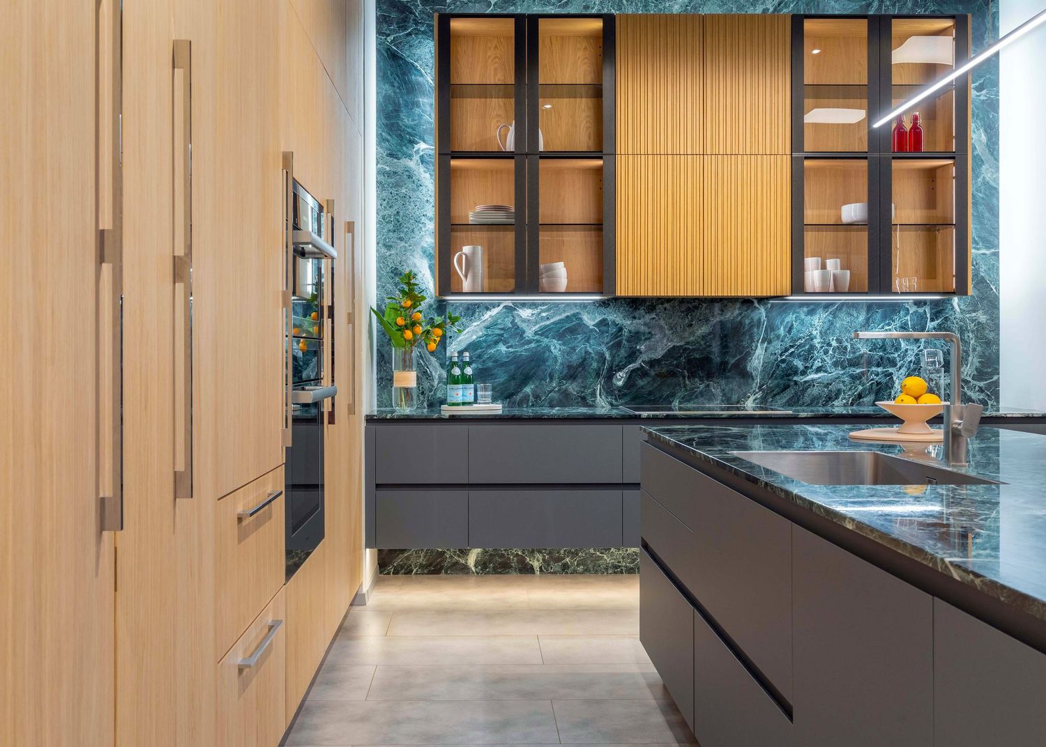 Modern kitchen with green marble backsplash, dark cabinetry, glass upper cabinets, and warm wood accents.