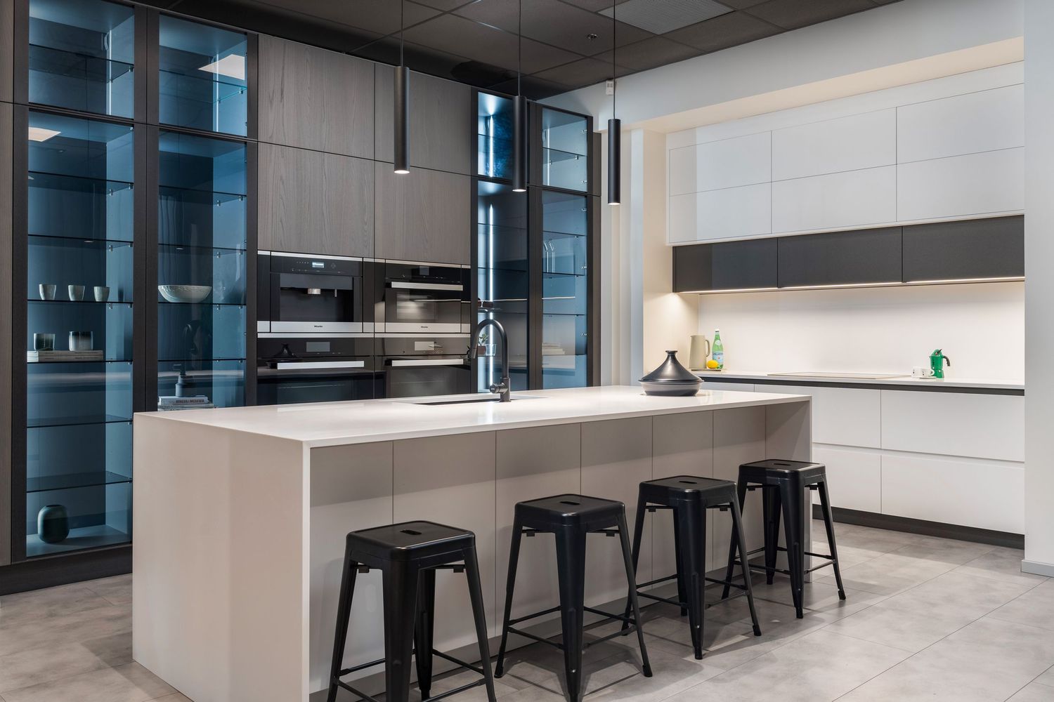 Modern office interior with sleek black bar stools along white counters and minimalist lighting design.
