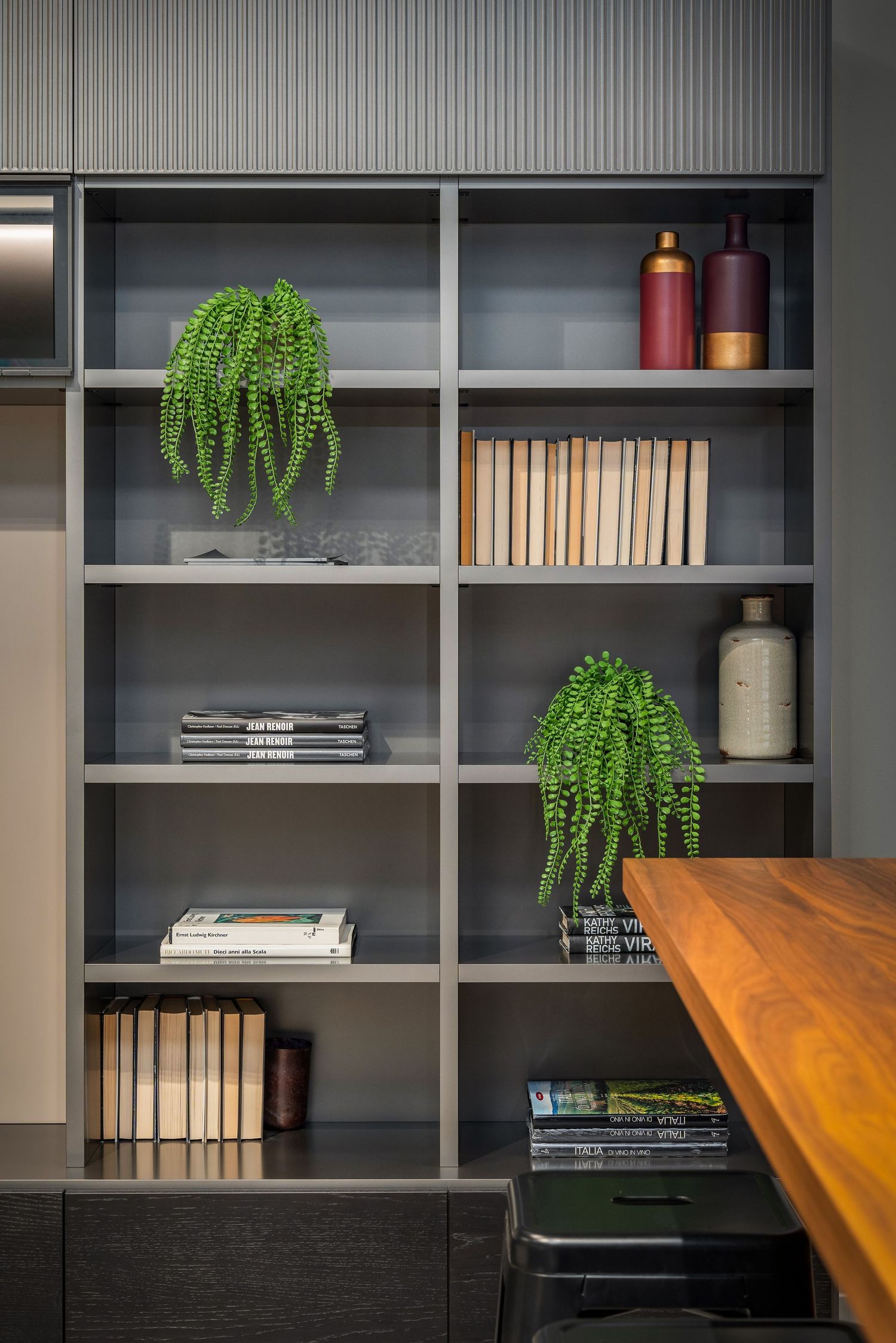 Modern gray bookshelf with trailing plants, books, and decorative vessels arranged neatly beside a wooden table.