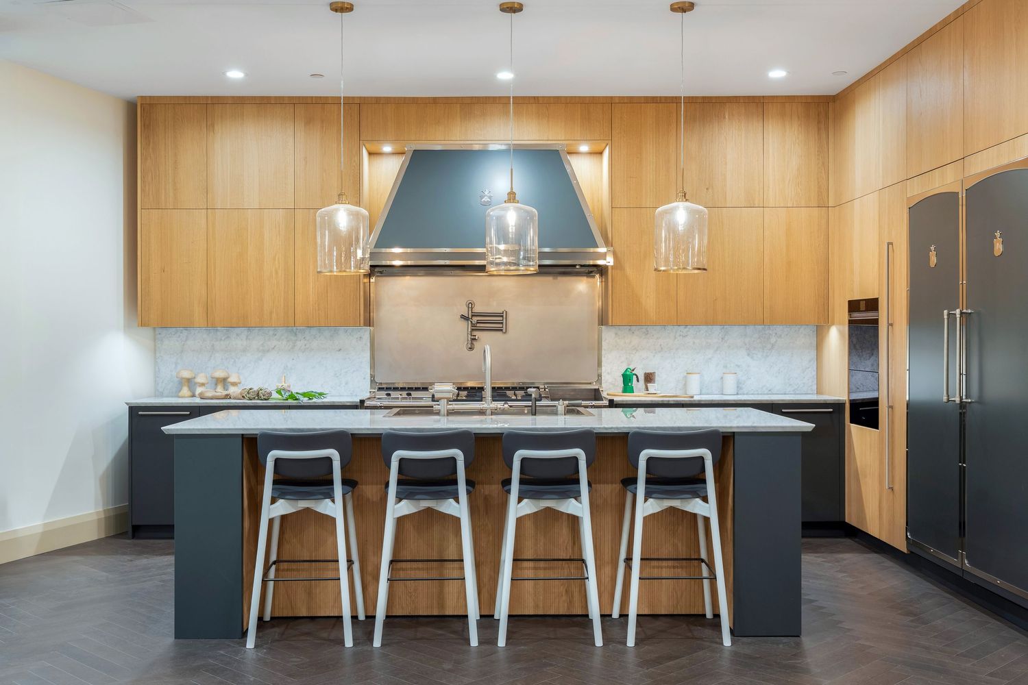 Modern kitchen with wooden cabinets, pendant lights, blue accents, and metal bar stools at the island counter.