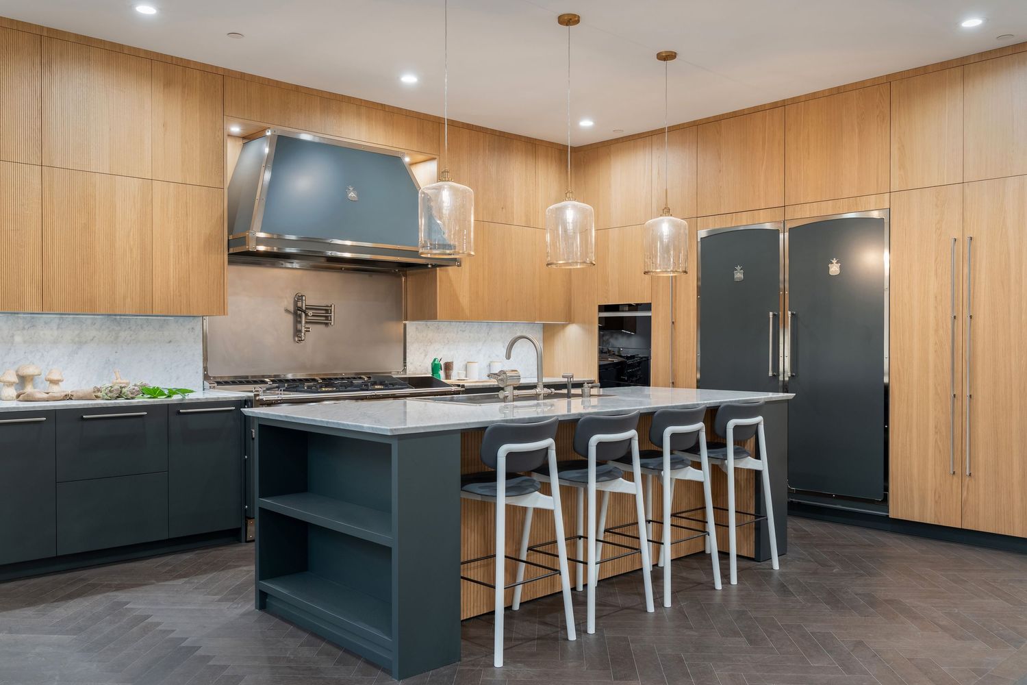 Modern kitchen with wood paneled walls, dark green cabinets, and metal bar stools at a long breakfast counter.