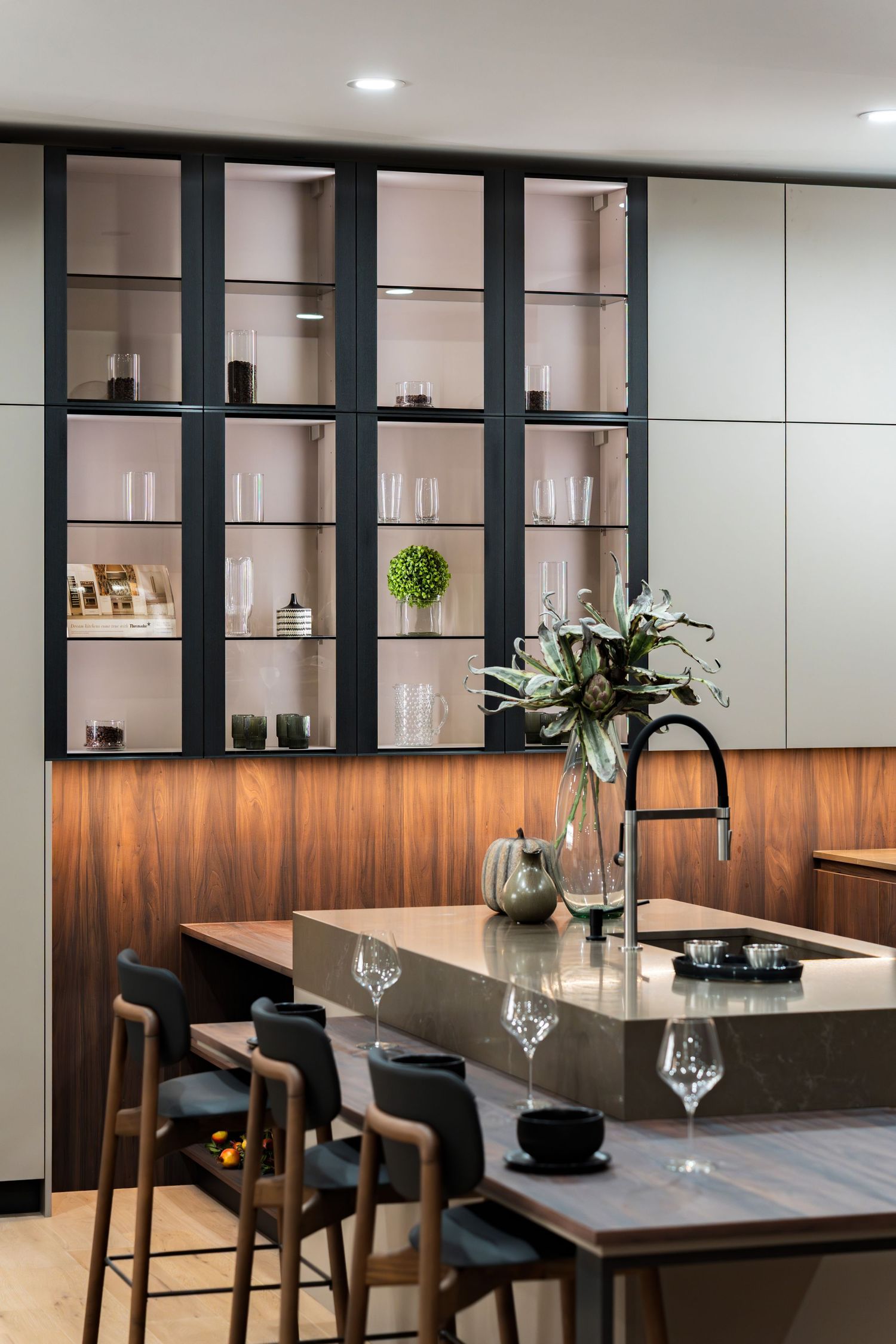 Modern dining area with built-in shelving, wood accents, and sleek black bar stools at a counter with wine glasses.
