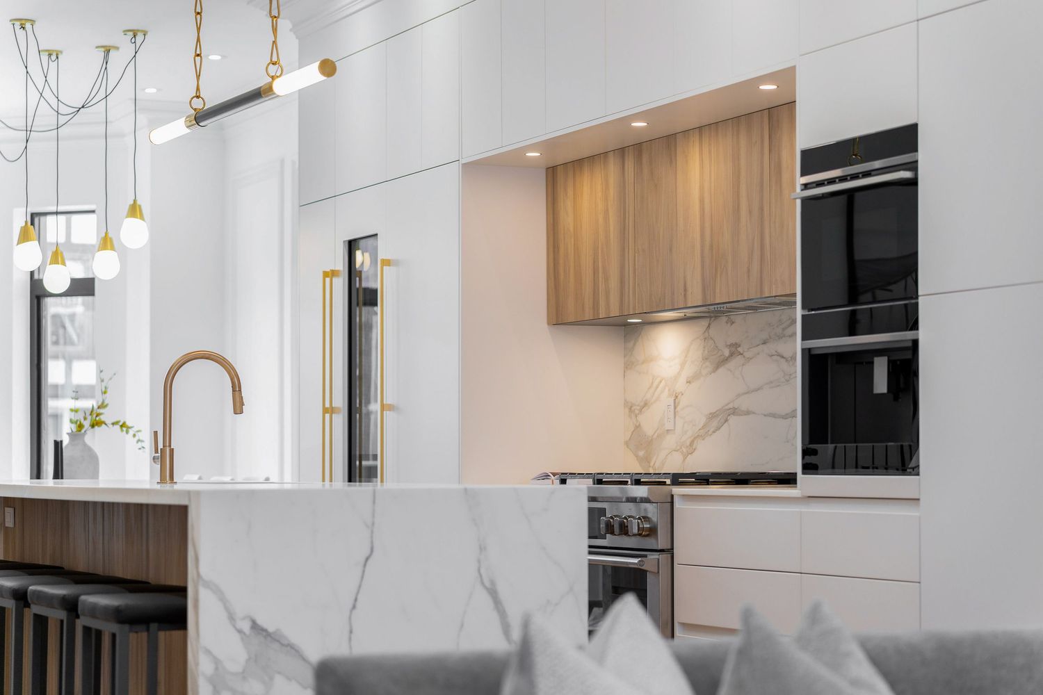 Modern white kitchen with gold pendant lights, wood cabinets, and marble backsplash features sleek minimalist design.