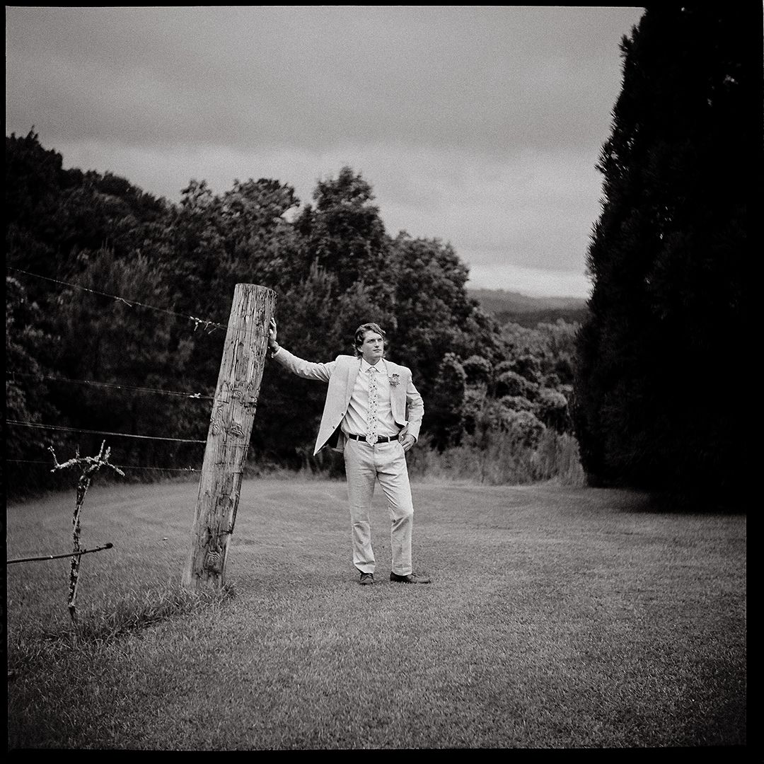 A black and white panoramic sequence showing two figures walking and posing near a wooden post in a grassy field.