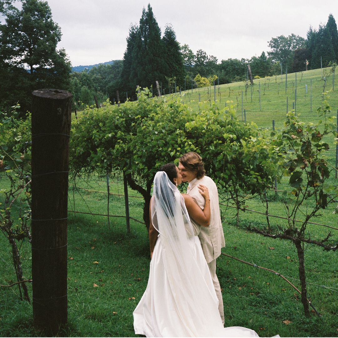 A couple embraces in a scenic vineyard with rolling hills and green grapevines stretching into the distance.