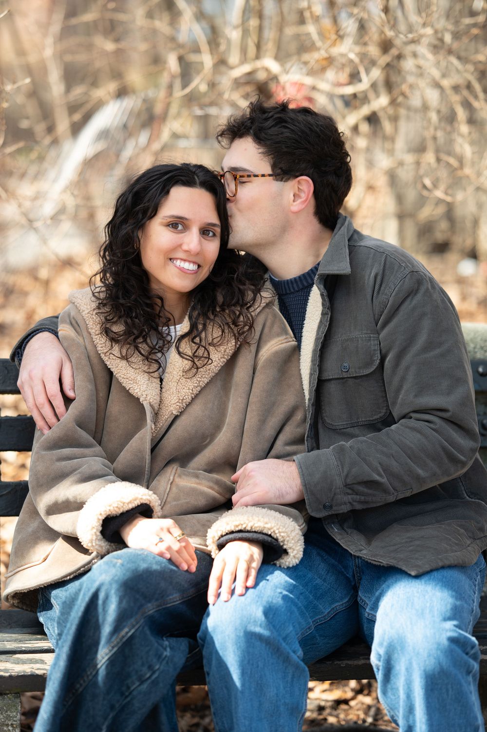A couple sitting on a bench shares an intimate moment together on an autumn day in casual attire.