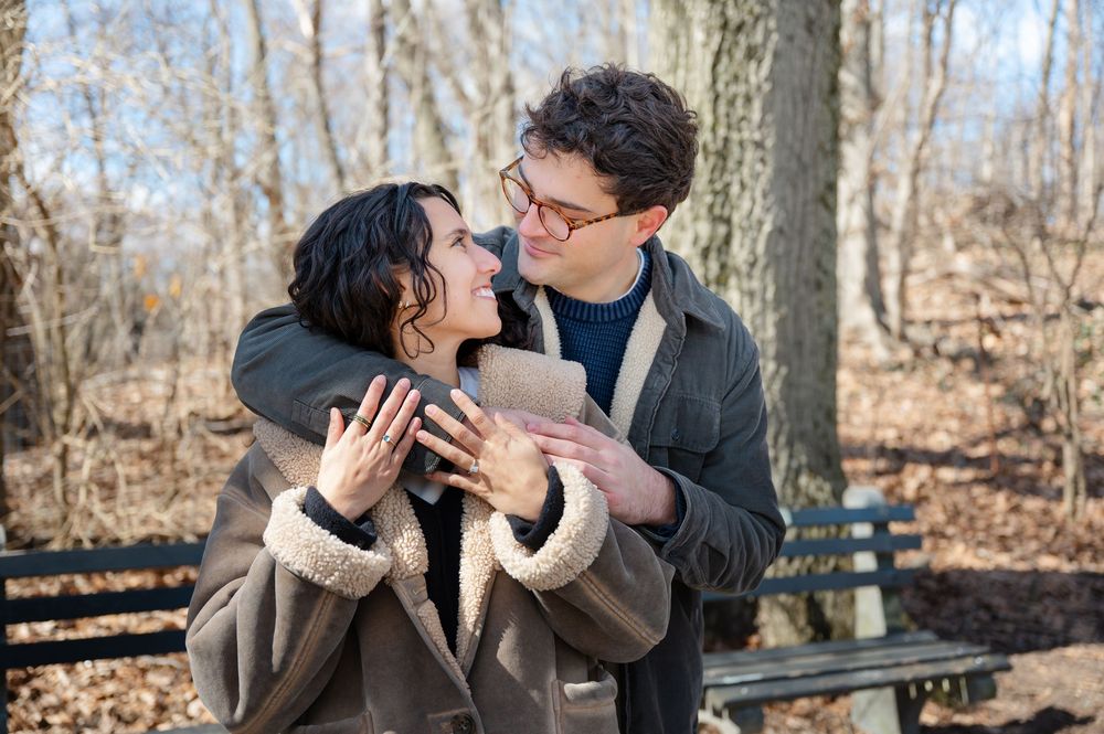 A couple shares romantic moments in a winter forest setting while sitting on a wooden bench.