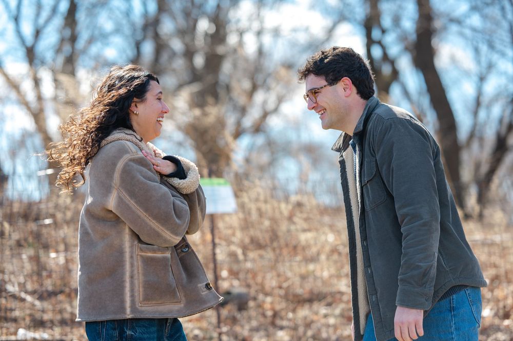 Couple walking and laughing together in a winter park with bare trees in the background in Prospect Park.