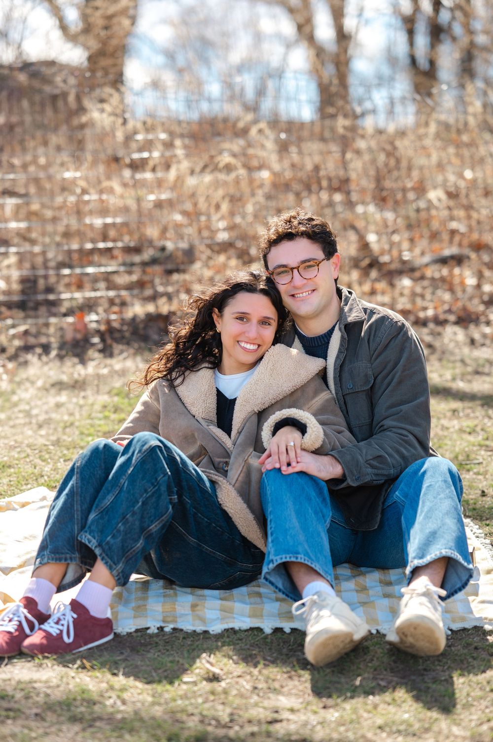 Couple lounging together on grass in casual outfits and sneakers during outdoor photo session.